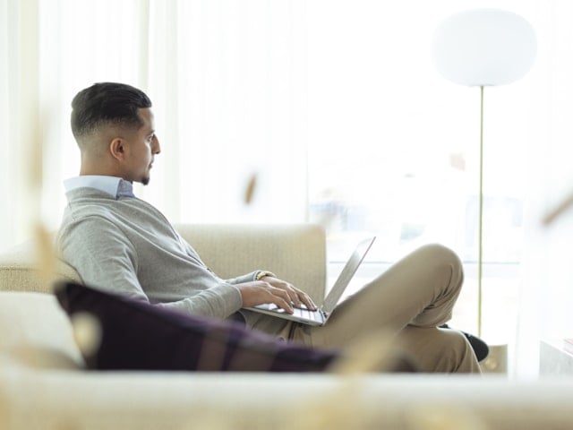 En man i en soffa med dator i sitt knä.