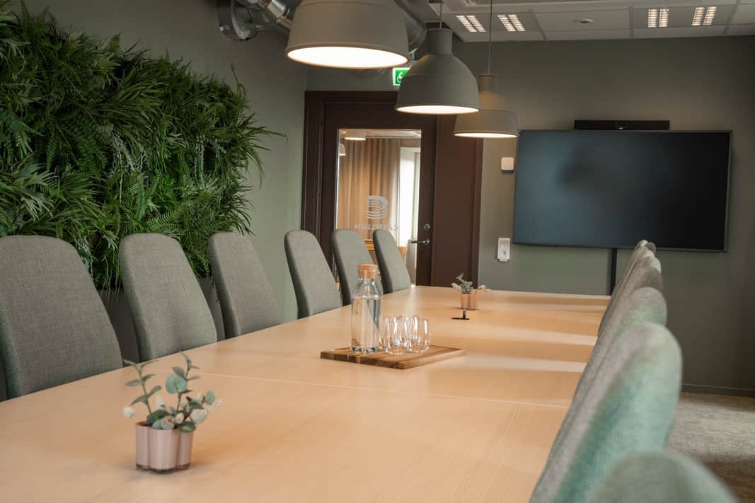 Ett större konferensrum med ljust bord och ljusgröna stolar