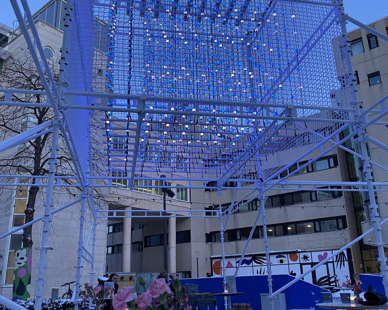 Ljusinstallation på byggställning med blomma i vas i förgrunden