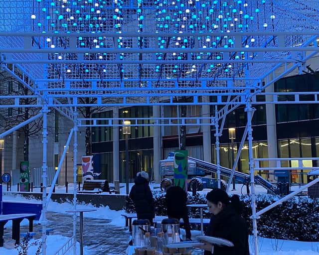 Ljusinstallation på byggställning och kvinna som serverar mat ute