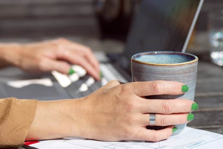 en hand som håller om en kopp och den andra vilar över ett tangentbord