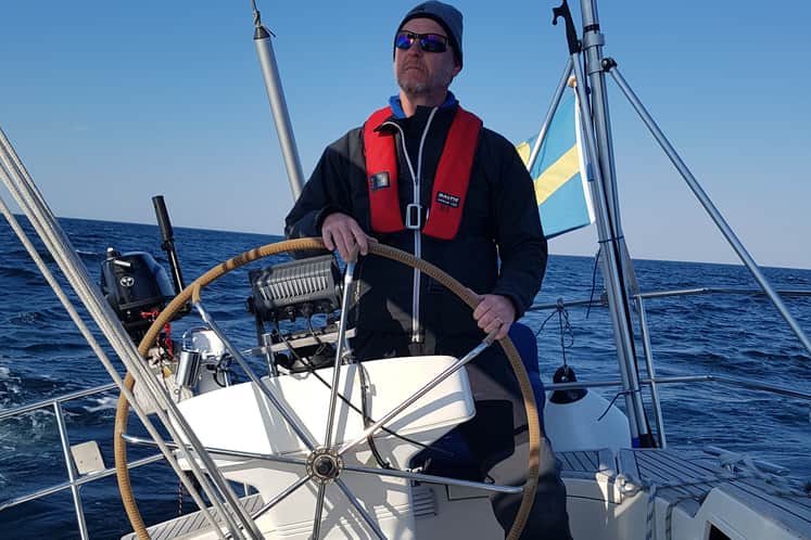 En man som står i en segelbåt och styr