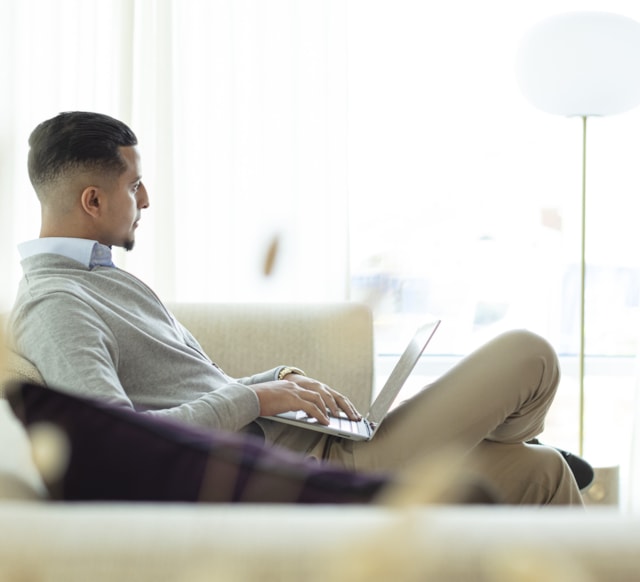 En man i en soffa med dator i sitt knä.