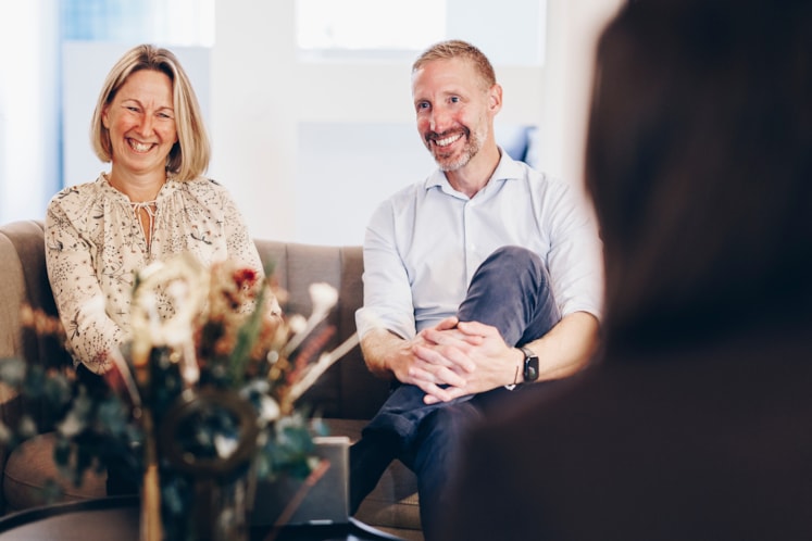 En man och en kvinna sitter och pratar i en soffa med en person mitt emot