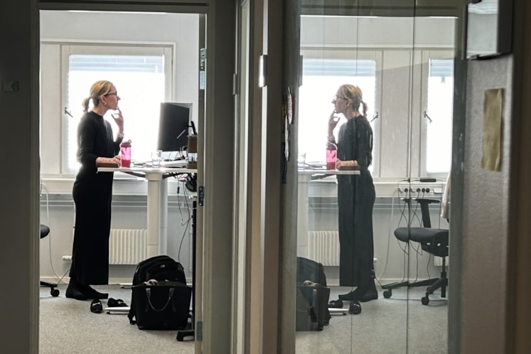 En person står på ett kontor och arbetar vid sitt skrivbord.