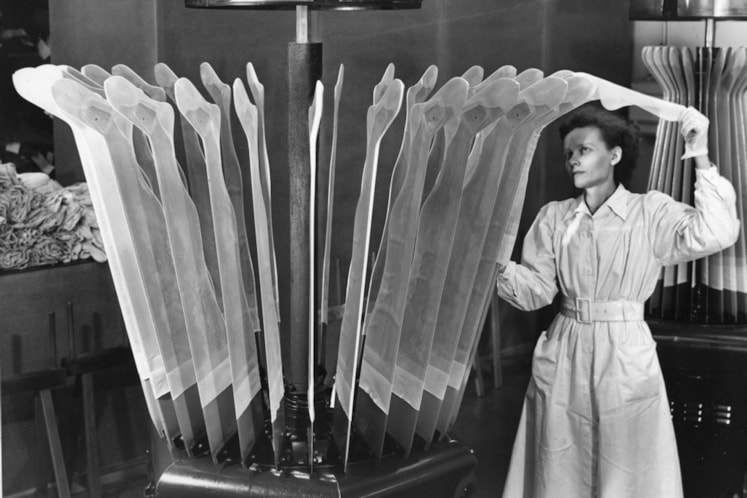 svartvitt foto, kvinna trär på strumpor, fabriksmiljö. 