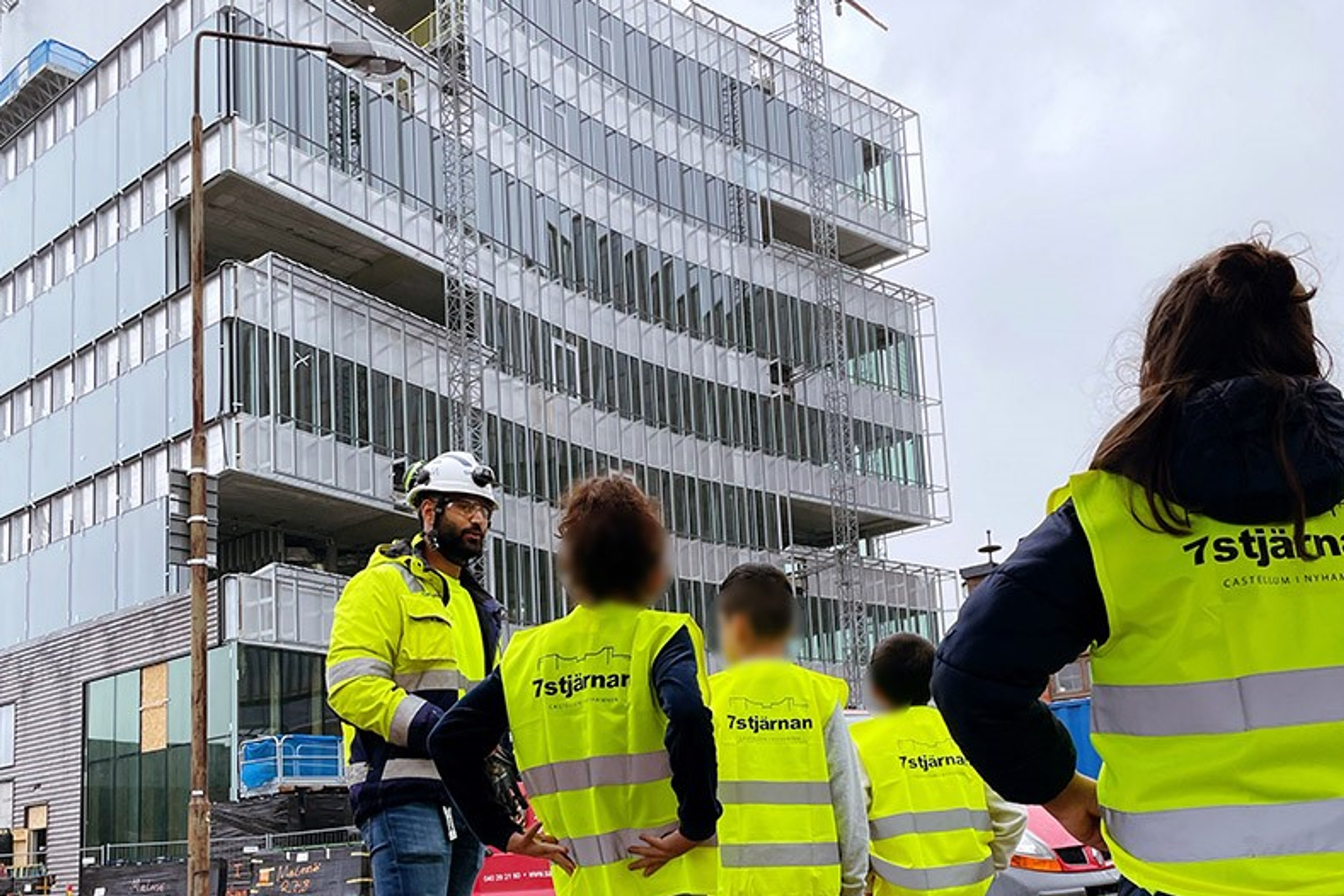 En grupp barn och vuxna i skyddsvästar framför byggprojektet.