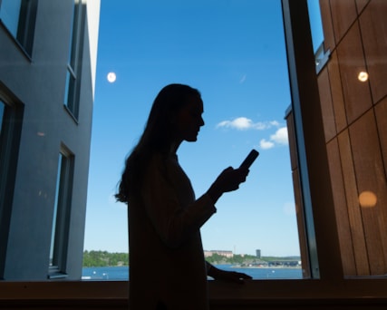 Person i fönster med en mobiltelefon i handen.